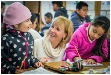 Woman smiling as she helps two girls with their writing.